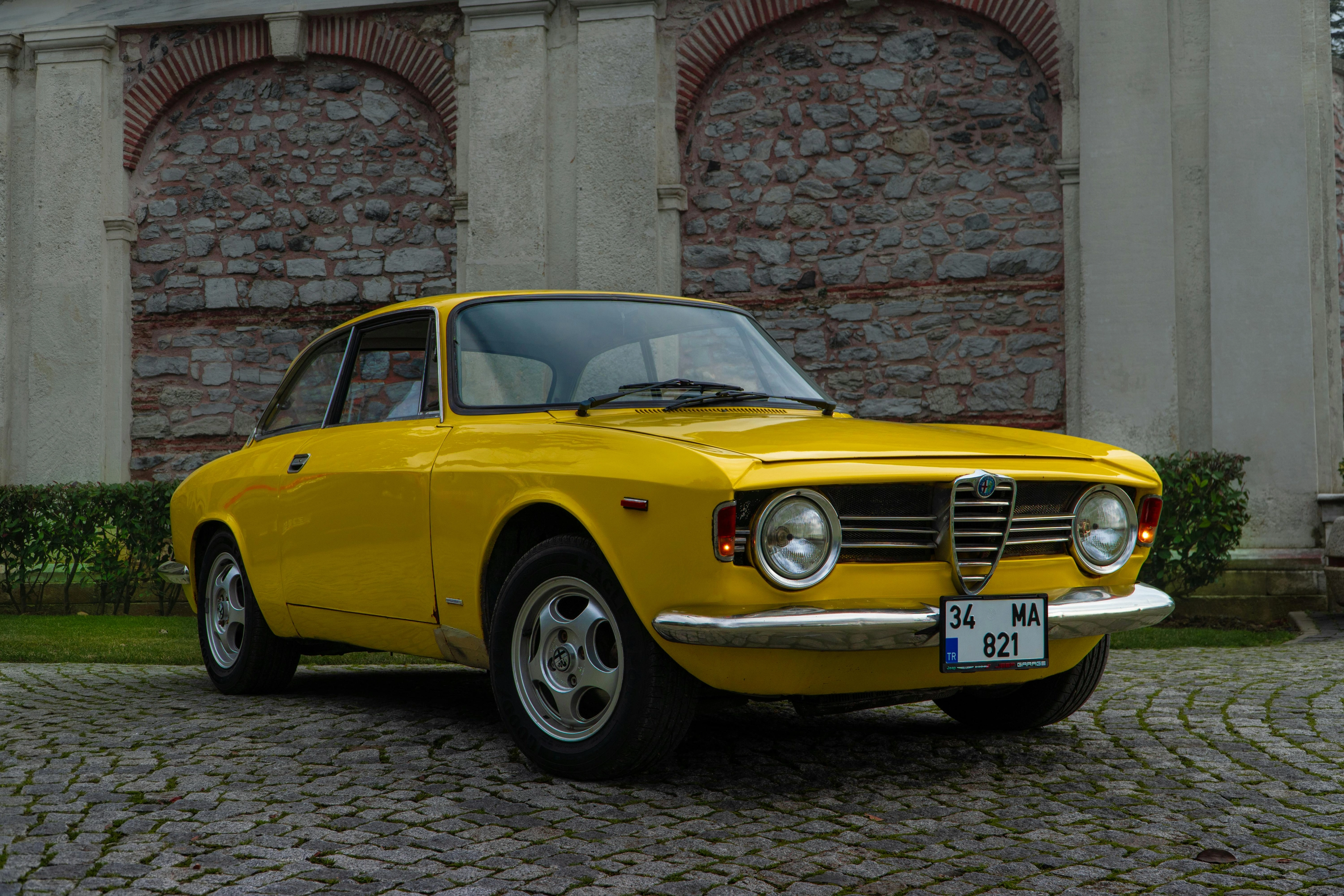 Klassischer gelber Alfa Romeo, geparkt auf Kopfsteinpflaster vor historischen Steinmauern.