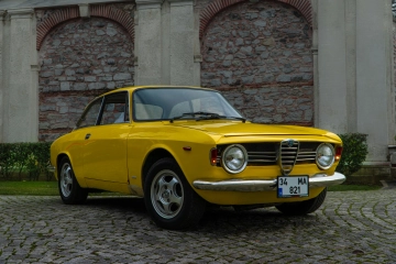 Klassischer gelber Alfa Romeo, geparkt auf Kopfsteinpflaster vor historischen Steinmauern.