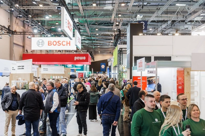 Eine belebte Messehalle mit vielen Besuchern, die zwischen den Ausstellungsständen umhergehen. Im Hintergrund sind Banner von verschiedenen Marken, darunter Bosch und pewo, sichtbar. Die Atmosphäre ist geschäftig und bunt.