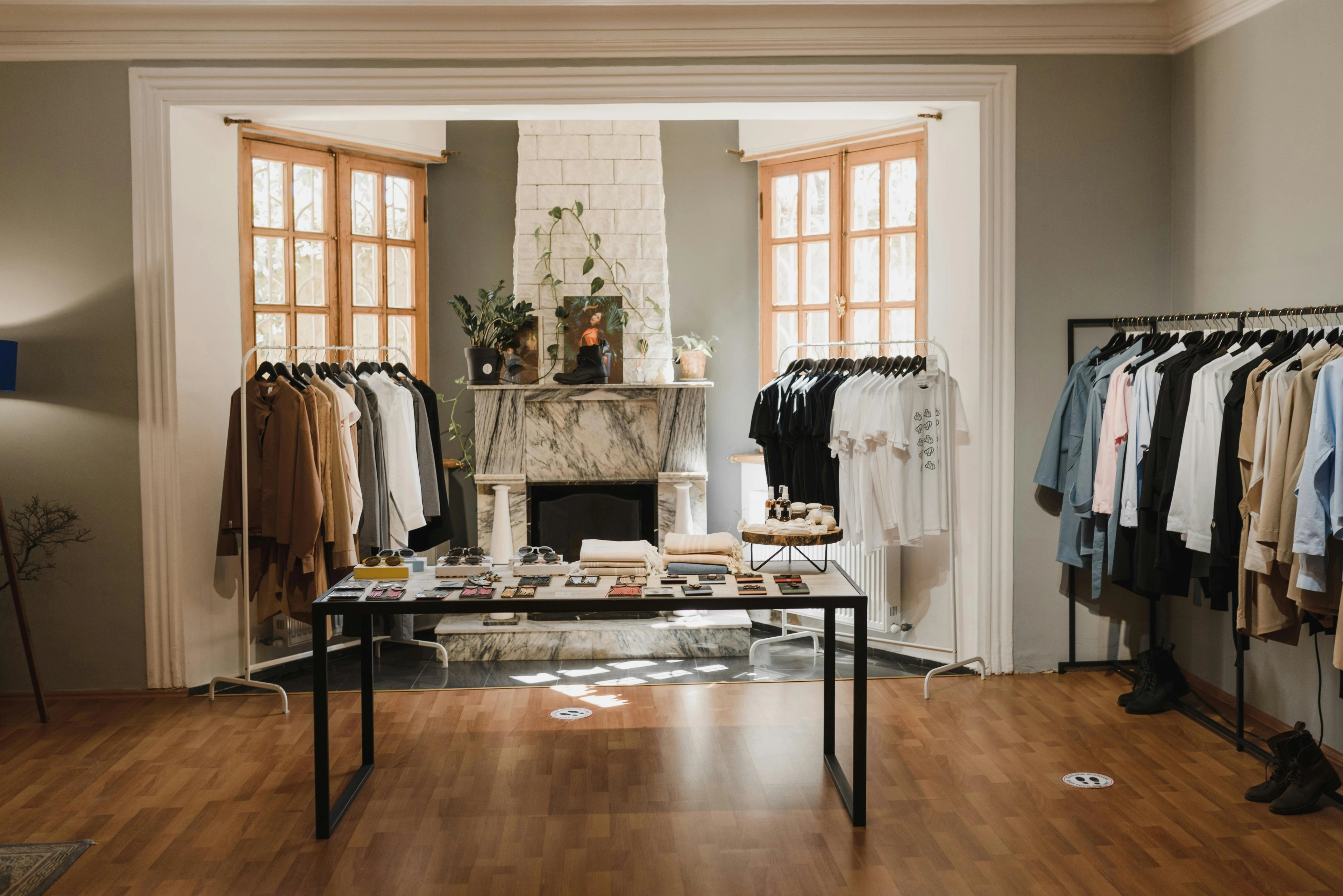 Modegeschäft/Showroom mit Kleiderstangen, Tisch mit Accessoires und einem Kamin im Hintergrund.