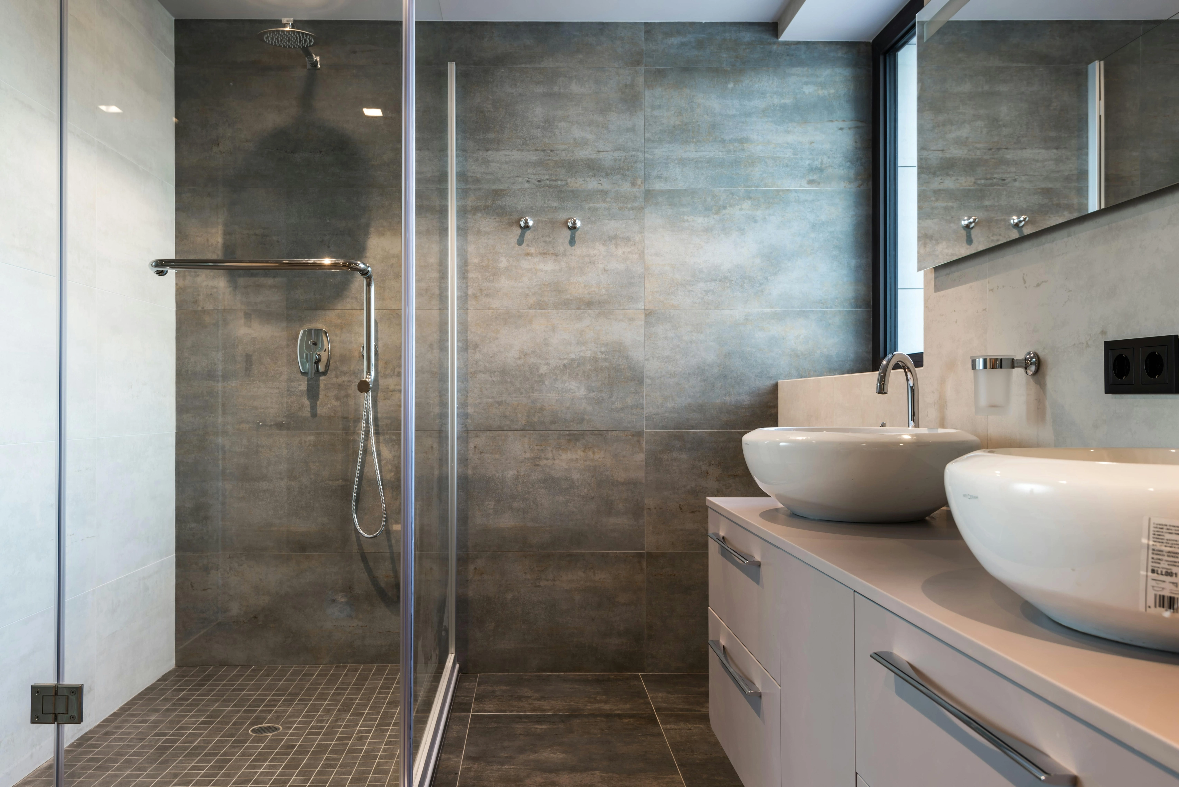 Modernes Badezimmer mit Glasdusche, Regendusche und zwei weißen Aufsatzwaschbecken auf Unterschrank.