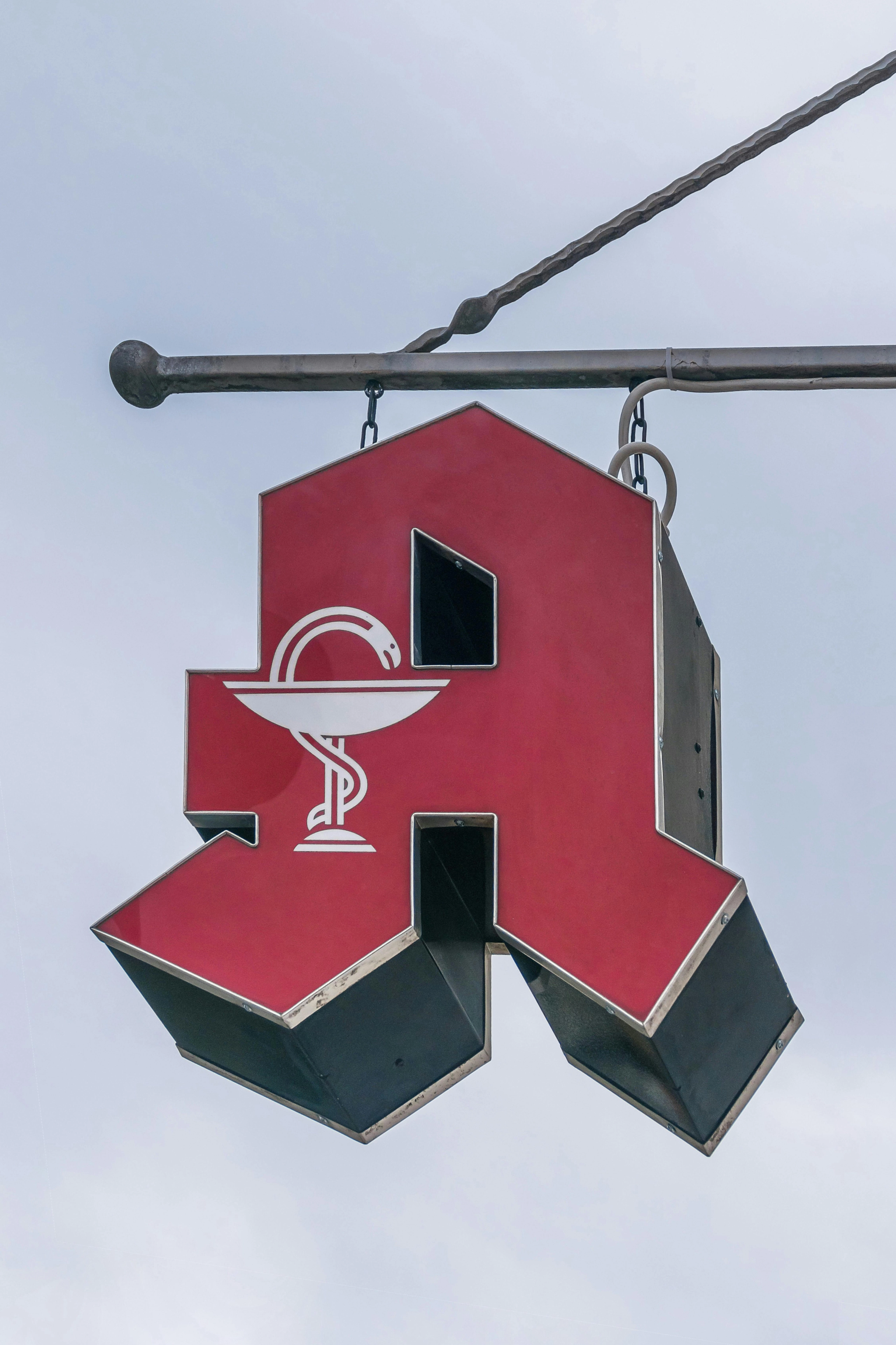 Rotes, hängendes Apotheken-Schild in Form eines großen A mit dem Schale-und-Schlange-Symbol.