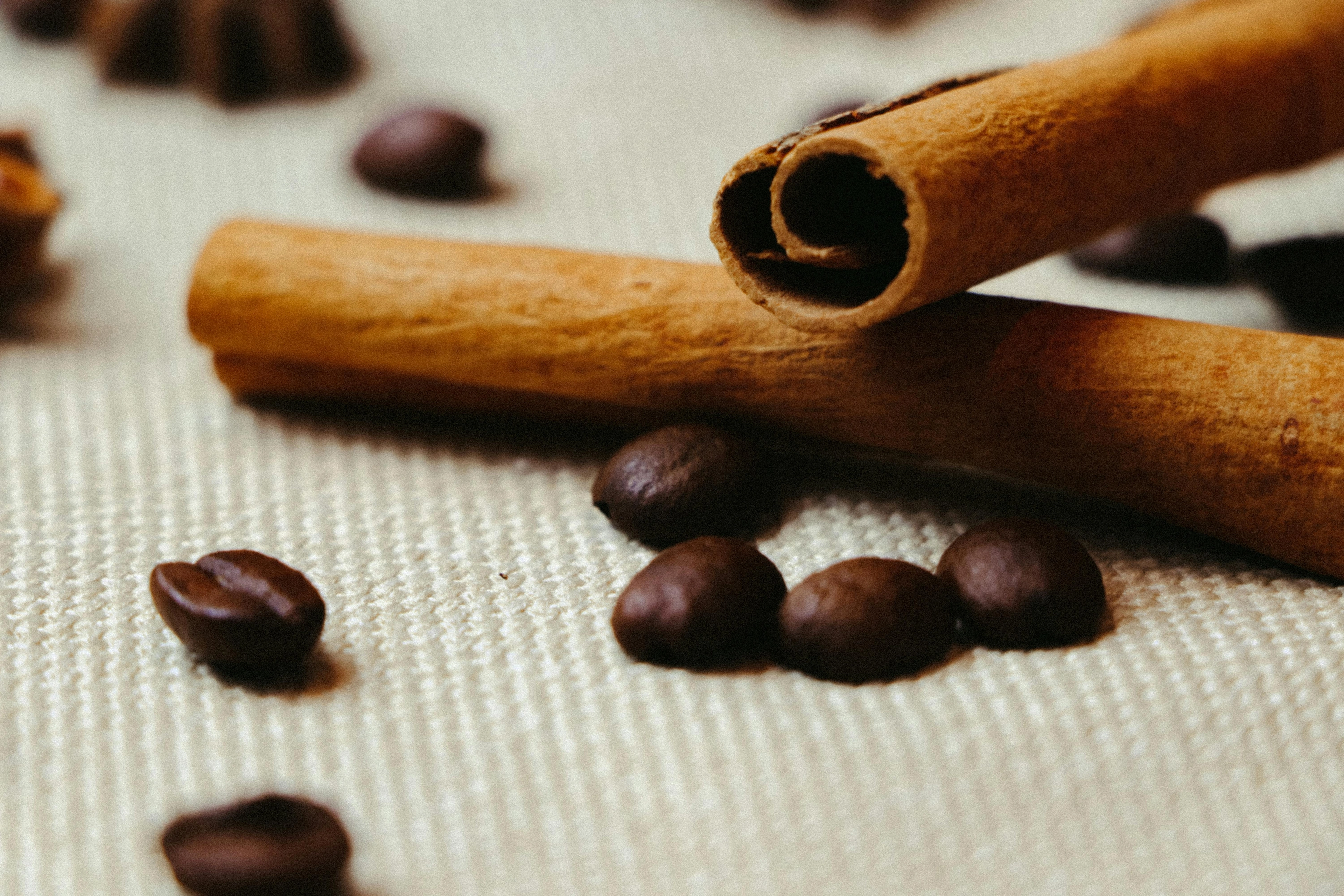 Nahaufnahme: zwei Zimtstangen und mehrere Kaffeebohnen auf hellem Stoff.