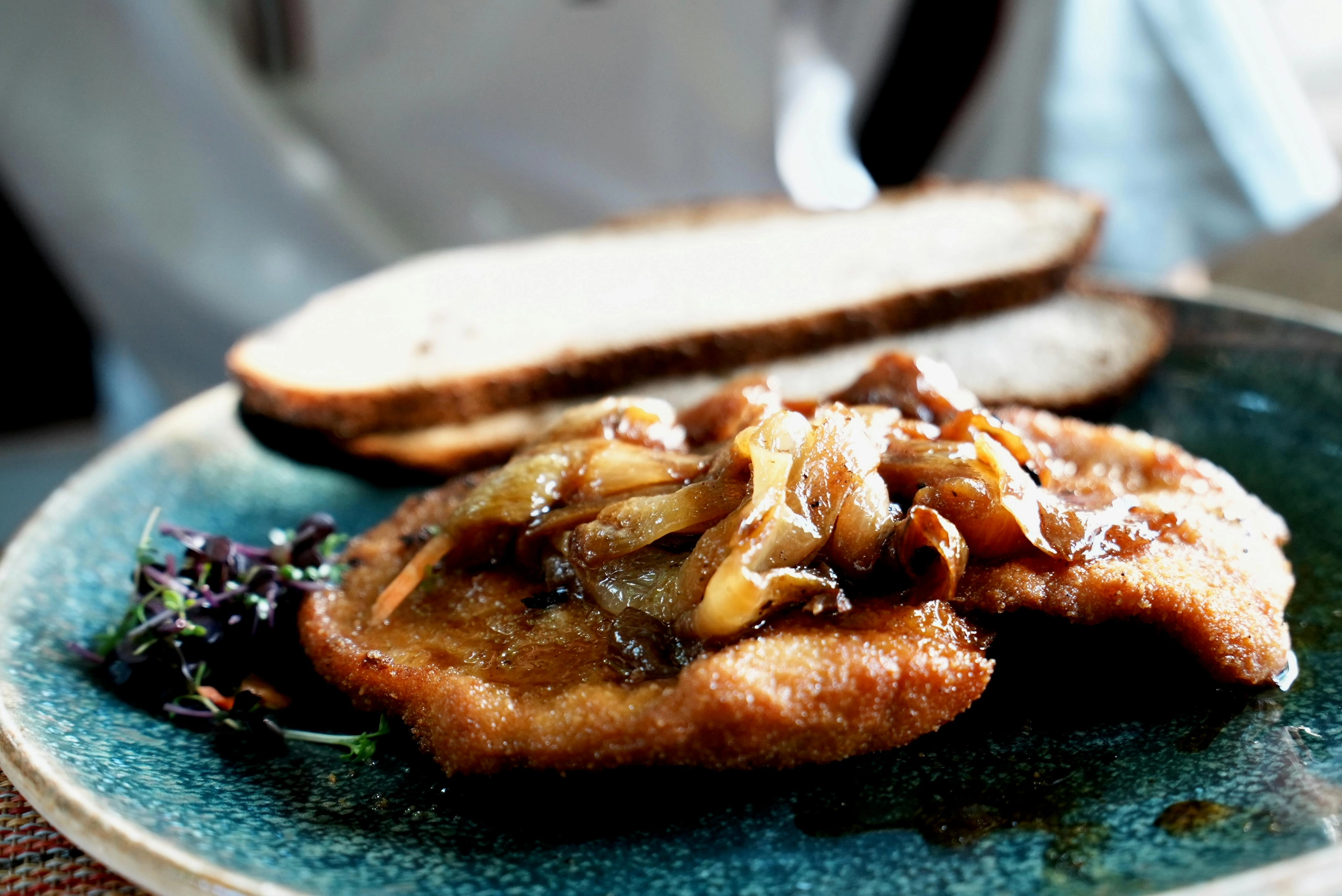 Teller mit paniertem Schnitzel, karamellisierten Zwiebeln und zwei Scheiben Brot.