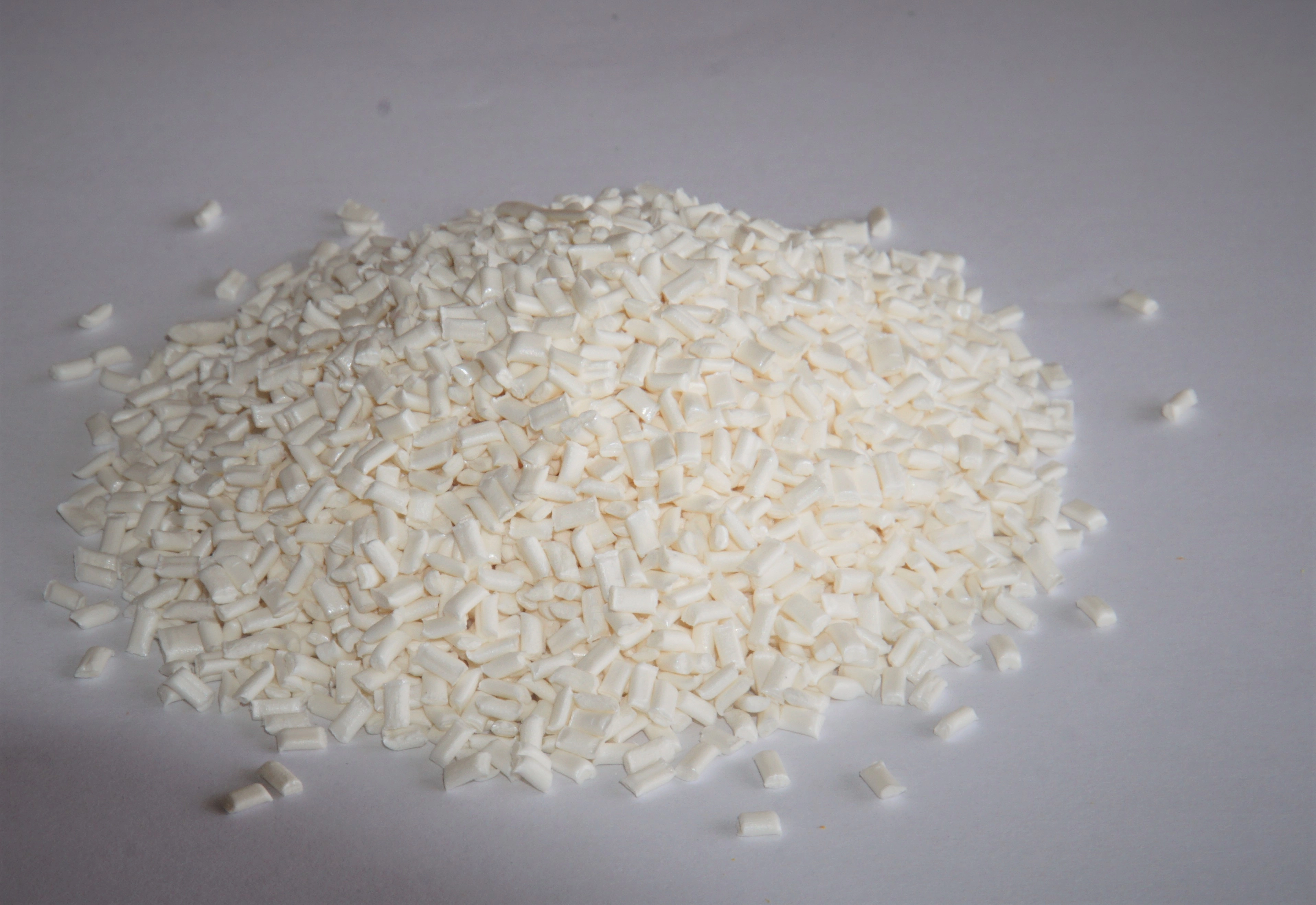 Haufen kleiner weißer Granulatpellets auf einem hellen Hintergrund.