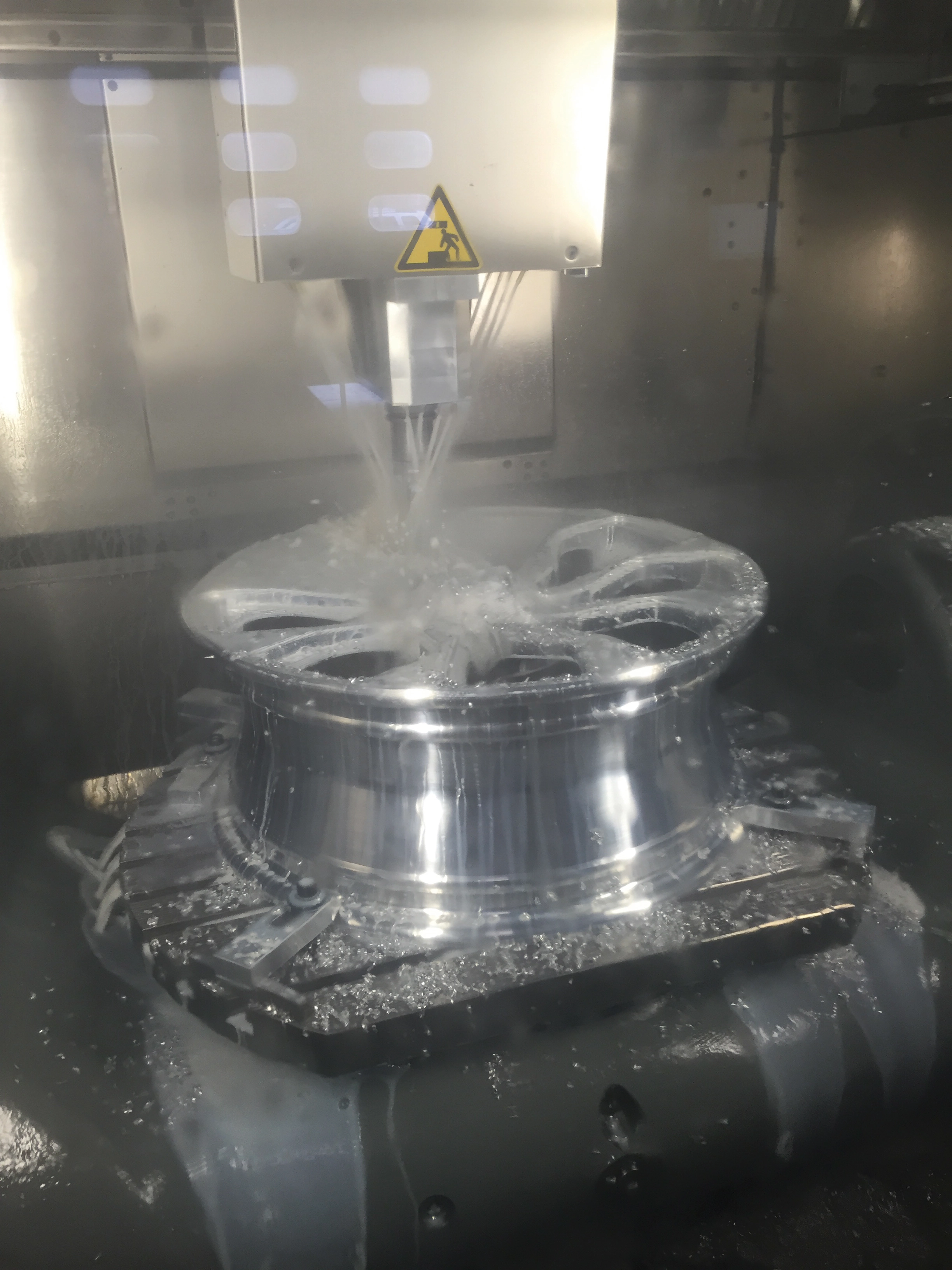 CNC-Fräsmaschine bearbeitet eine glänzende Metallfelge, Kühlmittel läuft über das Werkstück.