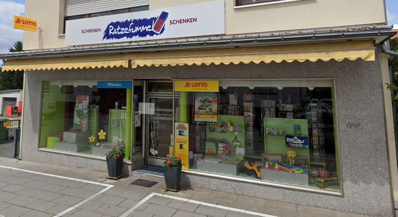 Außenansicht eines Schreibwaren- und Geschenkgeschäfts mit Schaufenstern, LOTTO-Logo und gelber Markise.