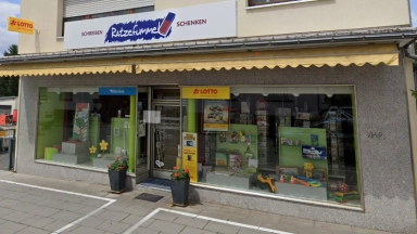 Außenansicht eines Schreibwaren- und Geschenkgeschäfts mit Schaufenstern, LOTTO-Logo und gelber Markise.