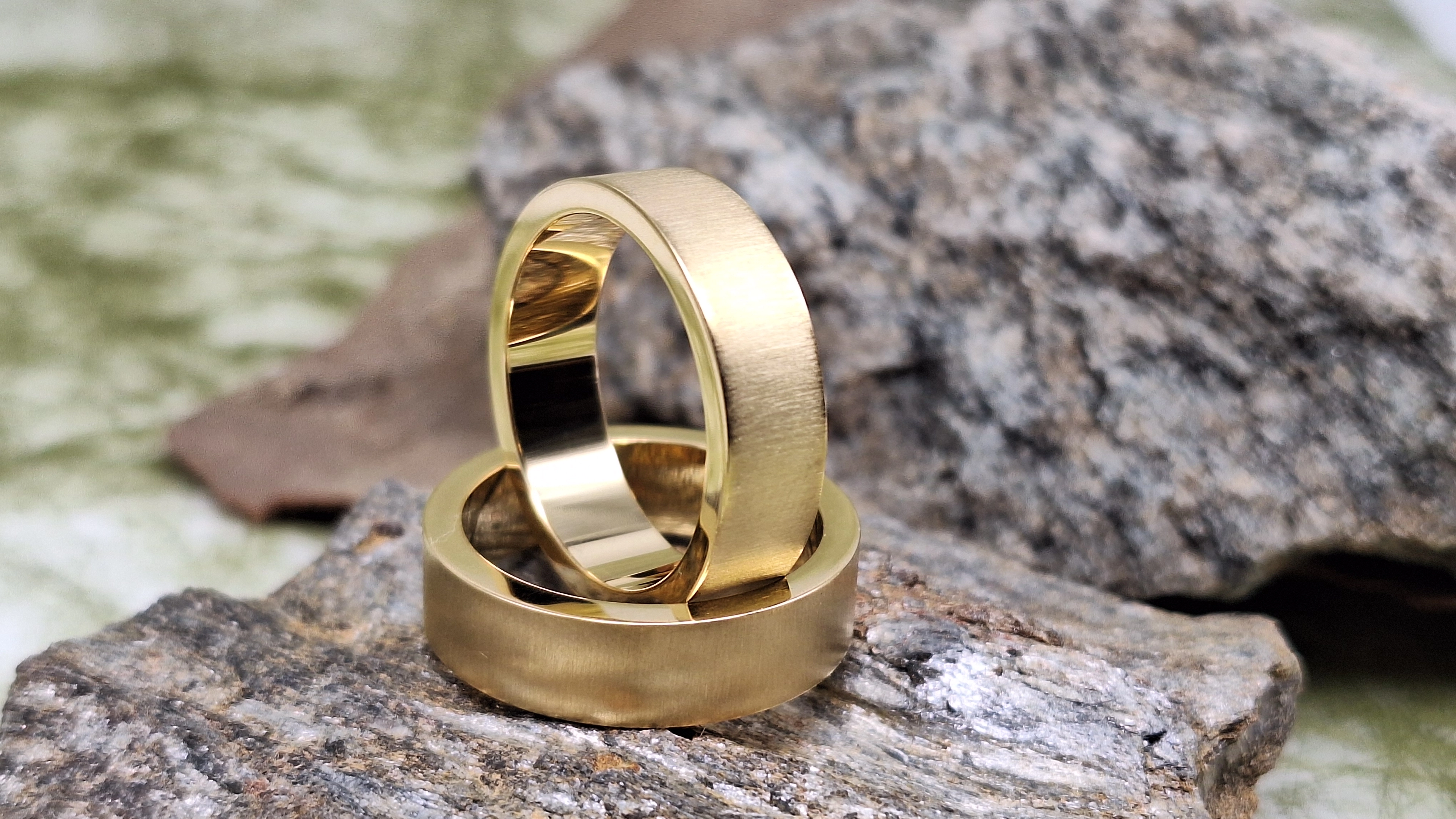 Nahaufnahme von zwei goldenen Ringen, die auf rauen grauen Steinen liegen.