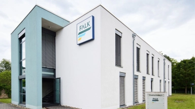 Zweistöckiges weißes Bürogebäude mit FALK-Logo an der Fassade, Eingangsbereich und Schildern auf dem Rasen.