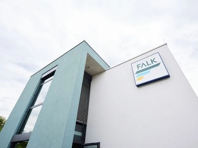 Fassade eines modernen Bürogebäudes mit großem FALK-Logo an der Wand vor bewölktem Himmel.