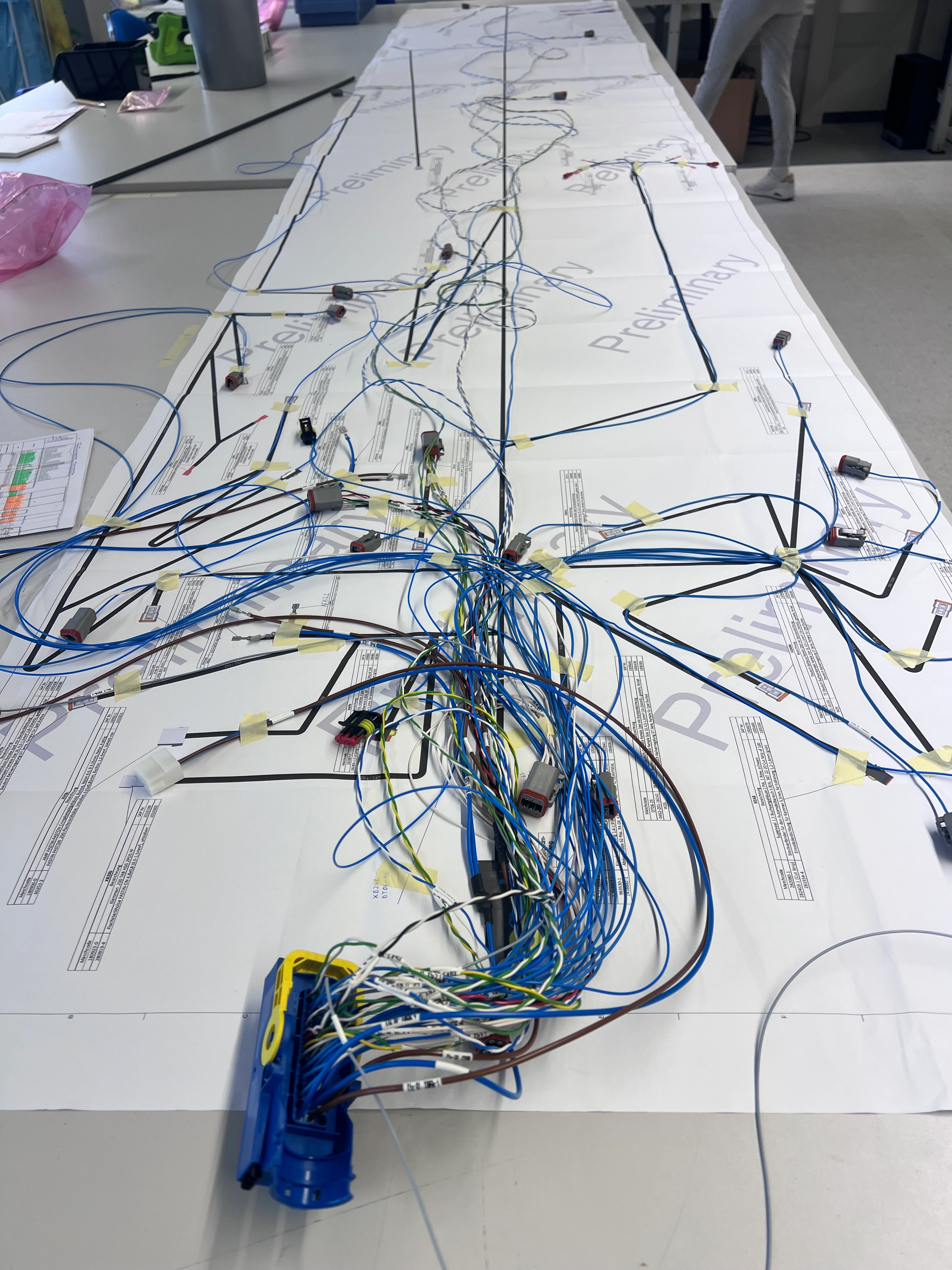 Langer Kabelbaum mit vielen blauen und bunten Drähten und Steckverbindern, ausgelegt auf Papierplänen auf einem Tisch.