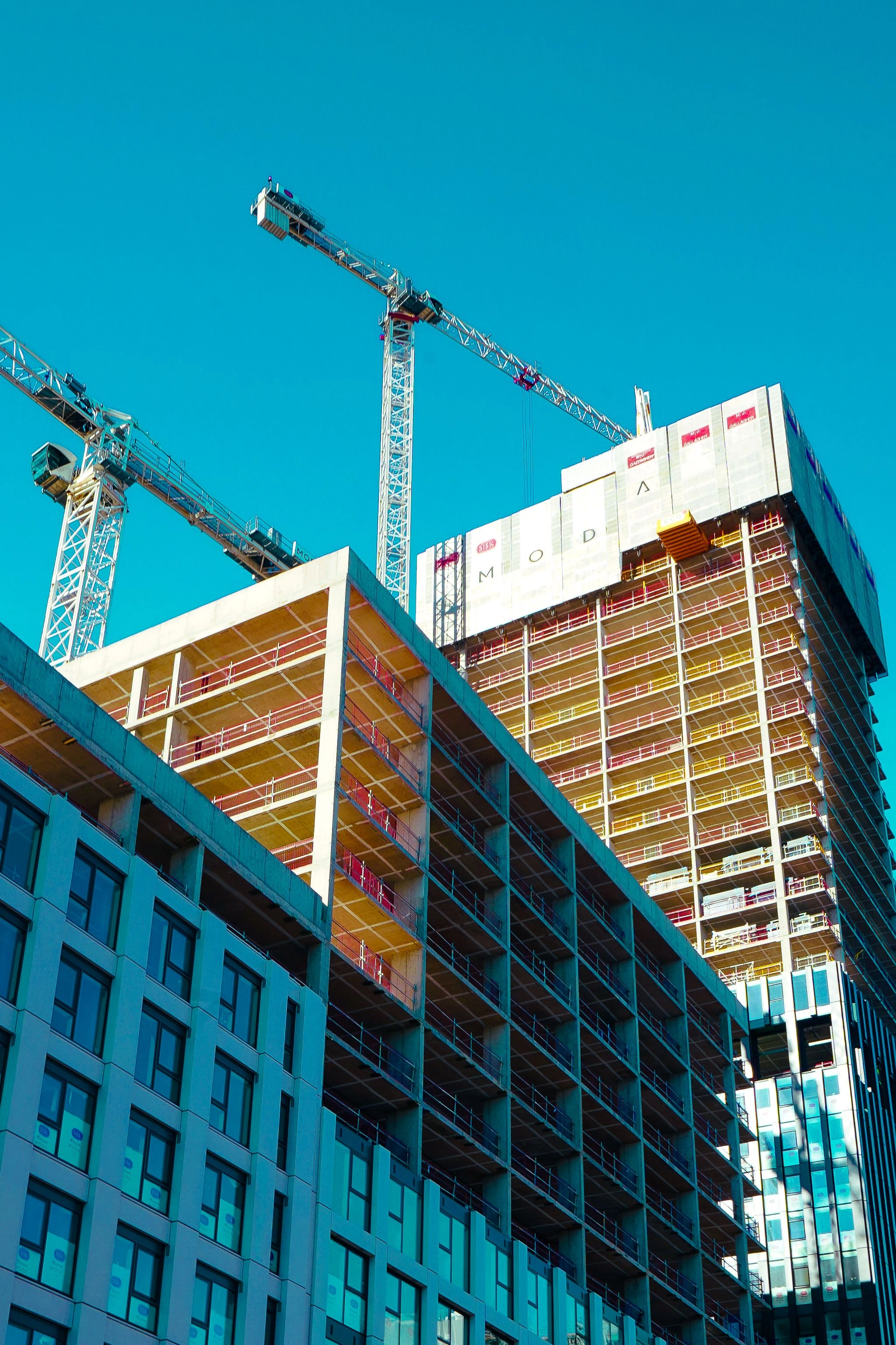 Mehrstöckiges Gebäude im Rohbau mit Gerüsten und zwei Baukränen vor klarem Himmel.