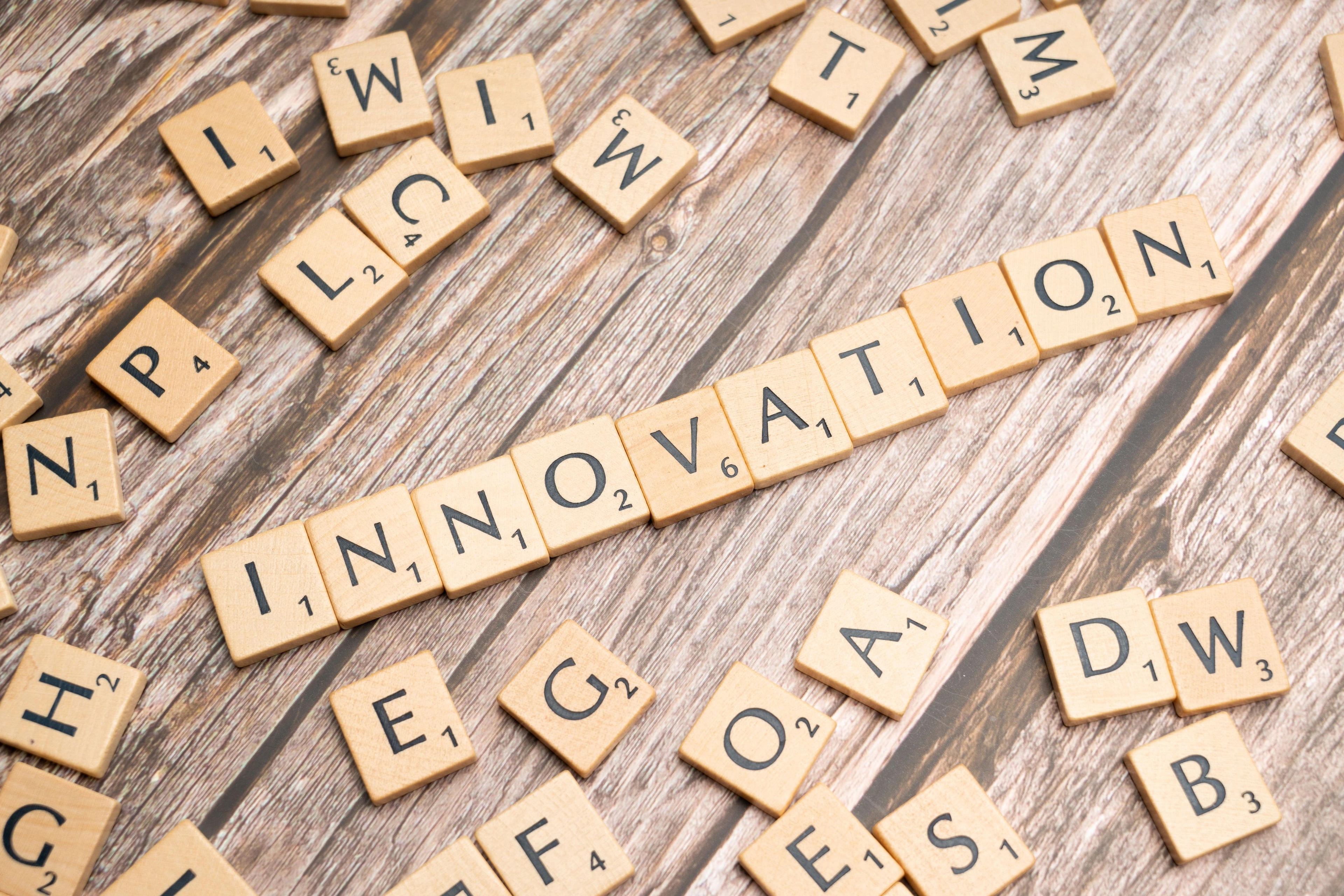 Buchstaben-Scrabble-Steine auf Holztisch, in einer Reihe das Wort ‚INNOVATION‘.