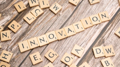 Buchstaben-Scrabble-Steine auf Holztisch, in einer Reihe das Wort ‚INNOVATION‘.