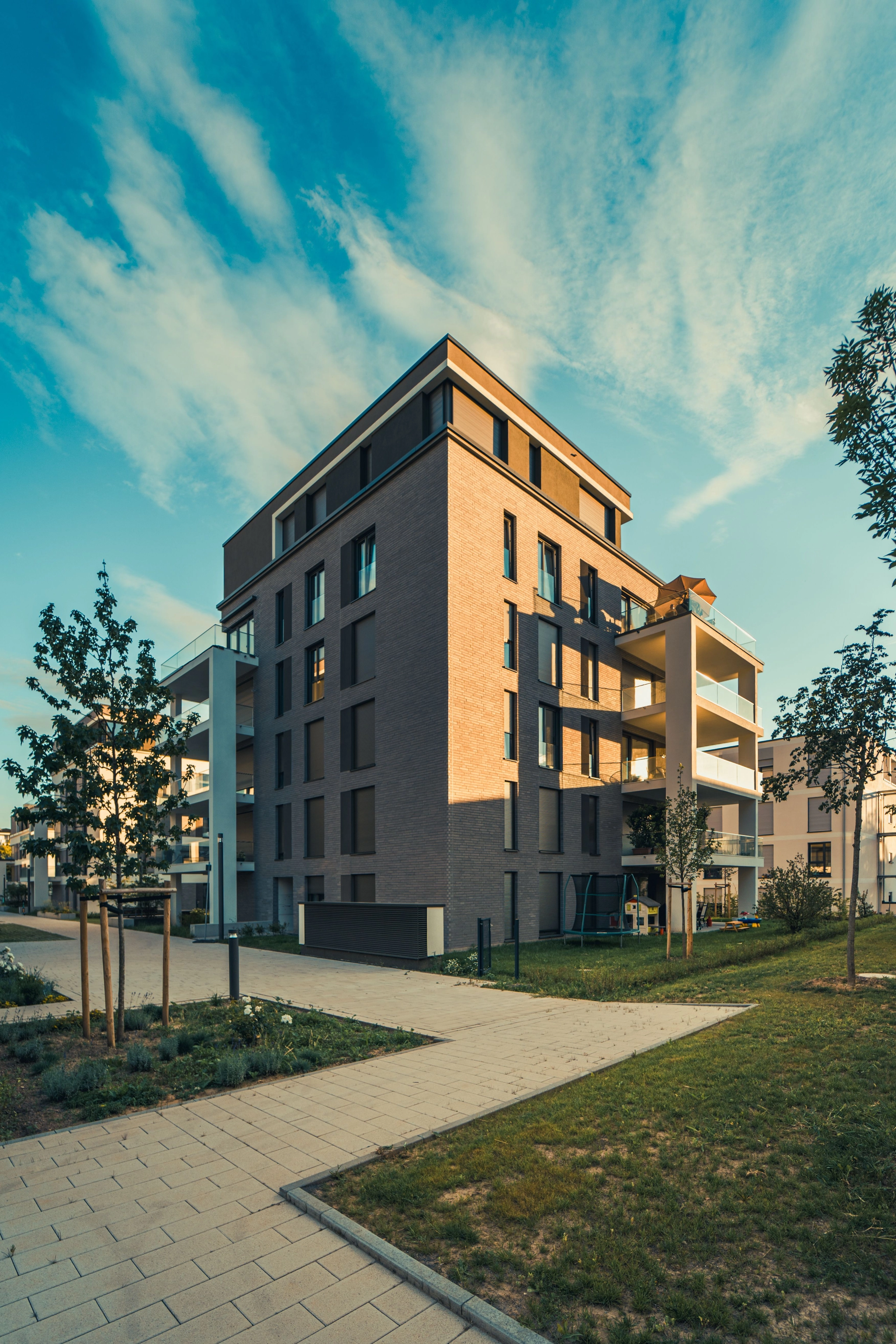 Mehrstöckiges modernes Wohngebäude mit Balkonen, Fußwegen und Rasenflächen unter blauem Himmel.