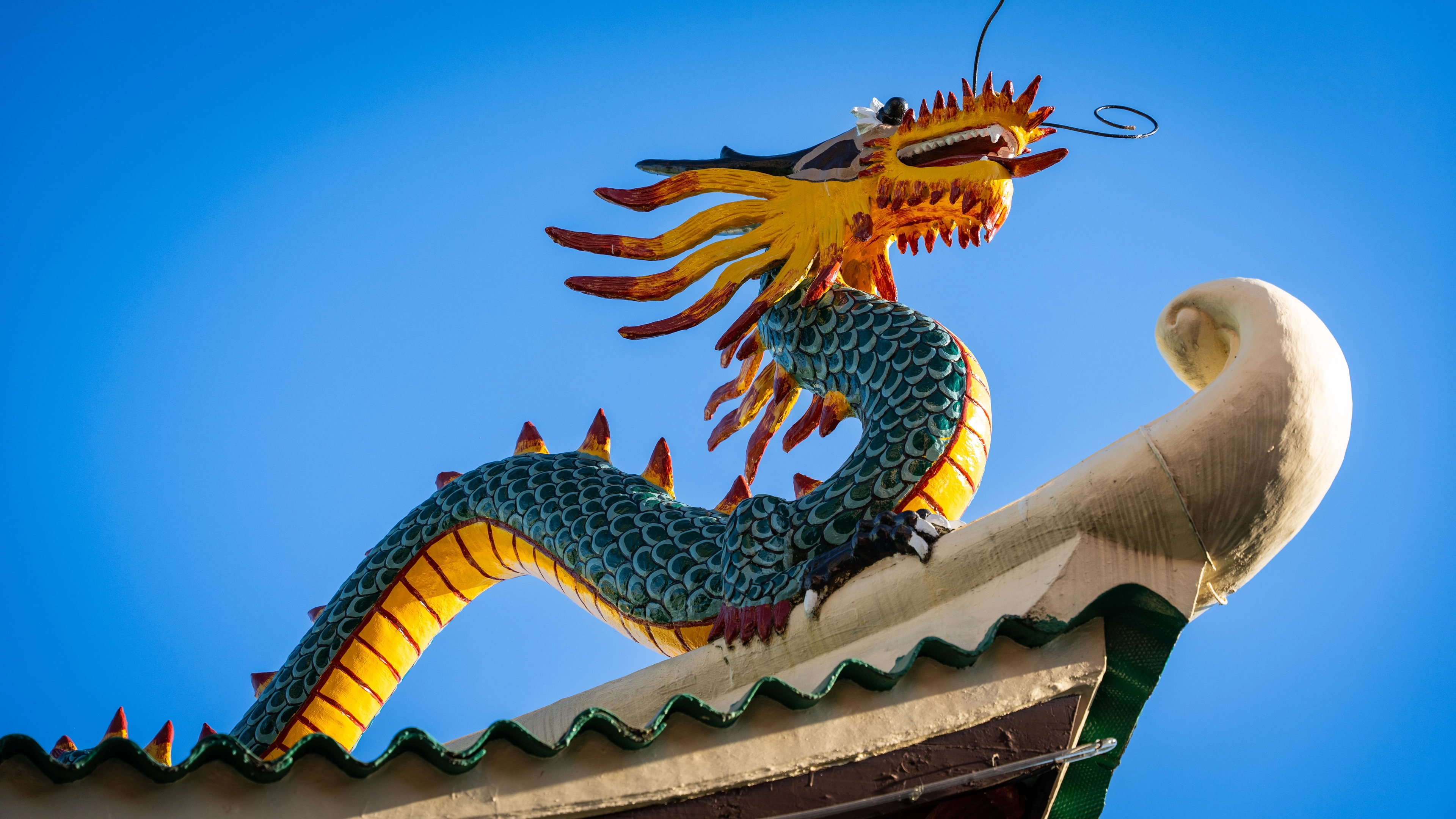 Bunte chinesische Drachenstatue auf dem Dachfirst vor klarem blauem Himmel.