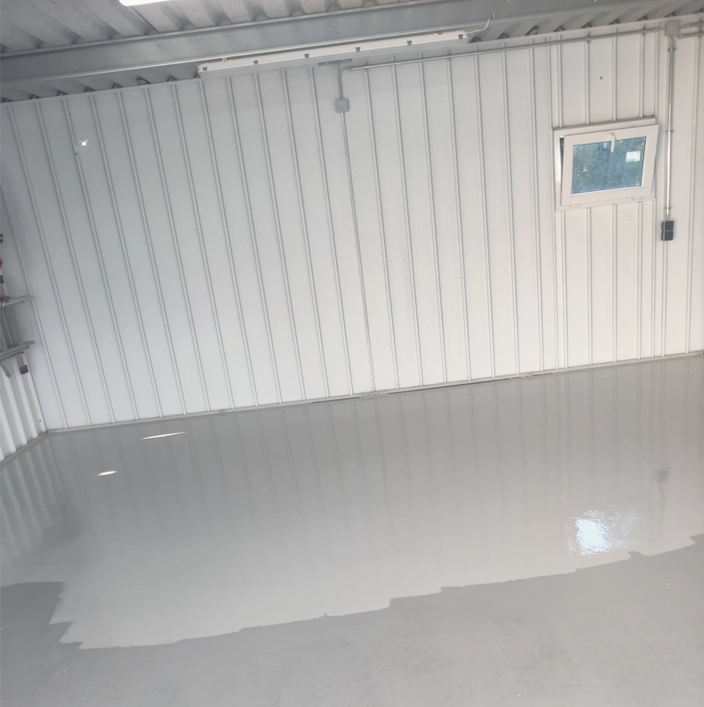 Leerer weißer Raum oder Garage mit glattem, frisch beschichtetem glänzendem Boden und kleinem Fenster in der Wand.