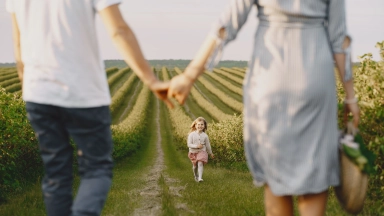 Ein Kind rennt auf seine Eltern zu, die sich auf einem Feldweg an den Händen halten.