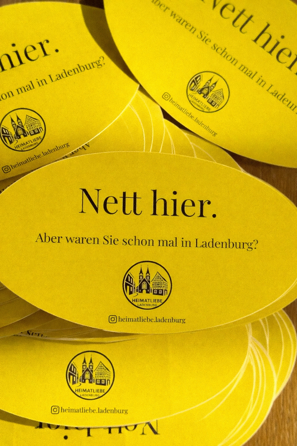 Mehrere gelbe ovale Werbekarten mit dem Text ‚Nett hier. Aber waren Sie schon mal in Ladenburg?‘ und einem kleinen Logo.