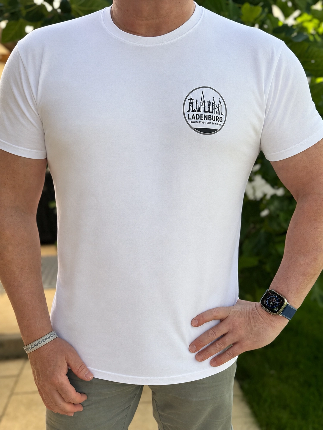Oberkörper einer erwachsenen Person in weißem T‑Shirt mit kleinem 'Ladenburg'-Logo links auf der Brust, mit Armband an der linken Hand und Smartwatch am rechten Handgelenk.