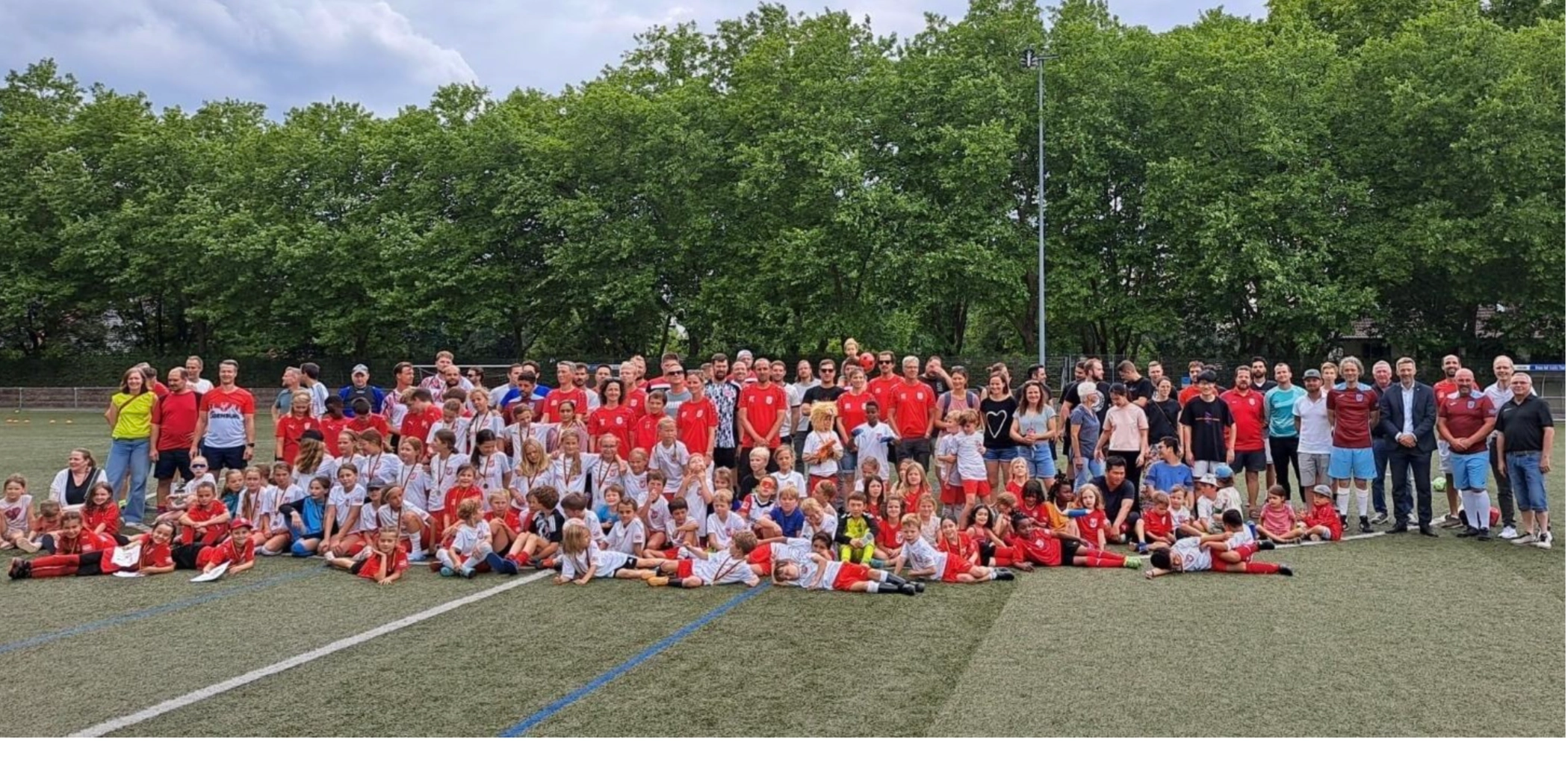 Große Gruppe von Kindern und erwachsenen Betreuern auf einem Sportplatz, posierend für ein Gruppenfoto.