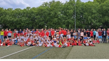 Große Gruppe von Kindern und erwachsenen Betreuern auf einem Sportplatz, posierend für ein Gruppenfoto.