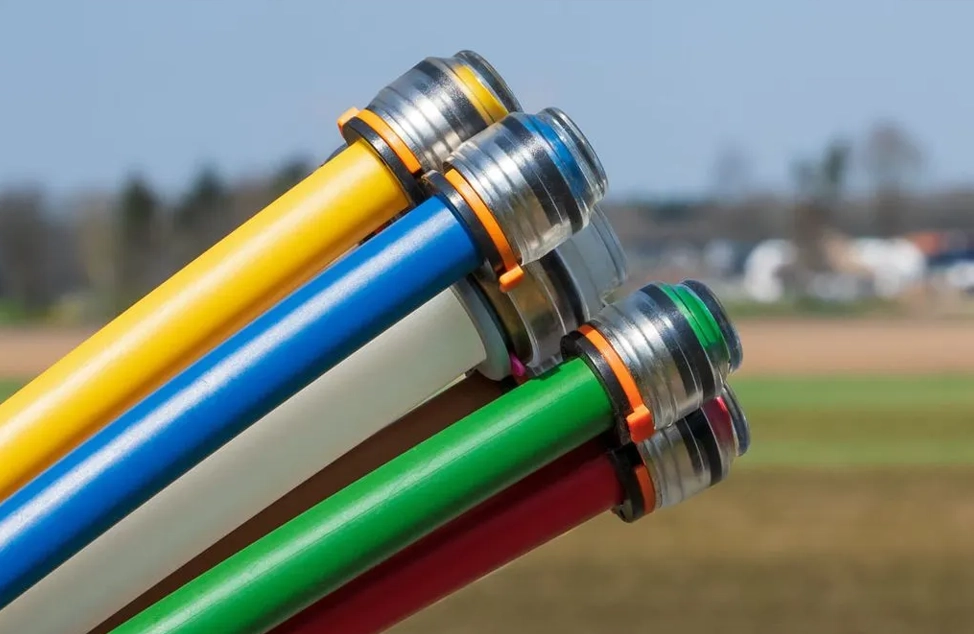 Nahaufnahme von mehreren bunten Stangen (gelb, blau, weiß, grün, rot) mit Metallringen und durchsichtigen Endkappen vor unscharfem Hintergrund.
