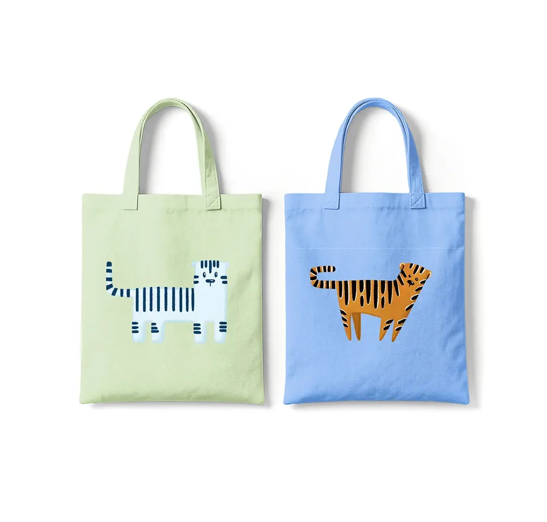 Zwei Stofftaschen nebeneinander: links hellgrün mit einem weiß-blau gestreiften Tiermotiv, rechts hellblau mit einem orange-schwarz gestreiften Tigermotiv.