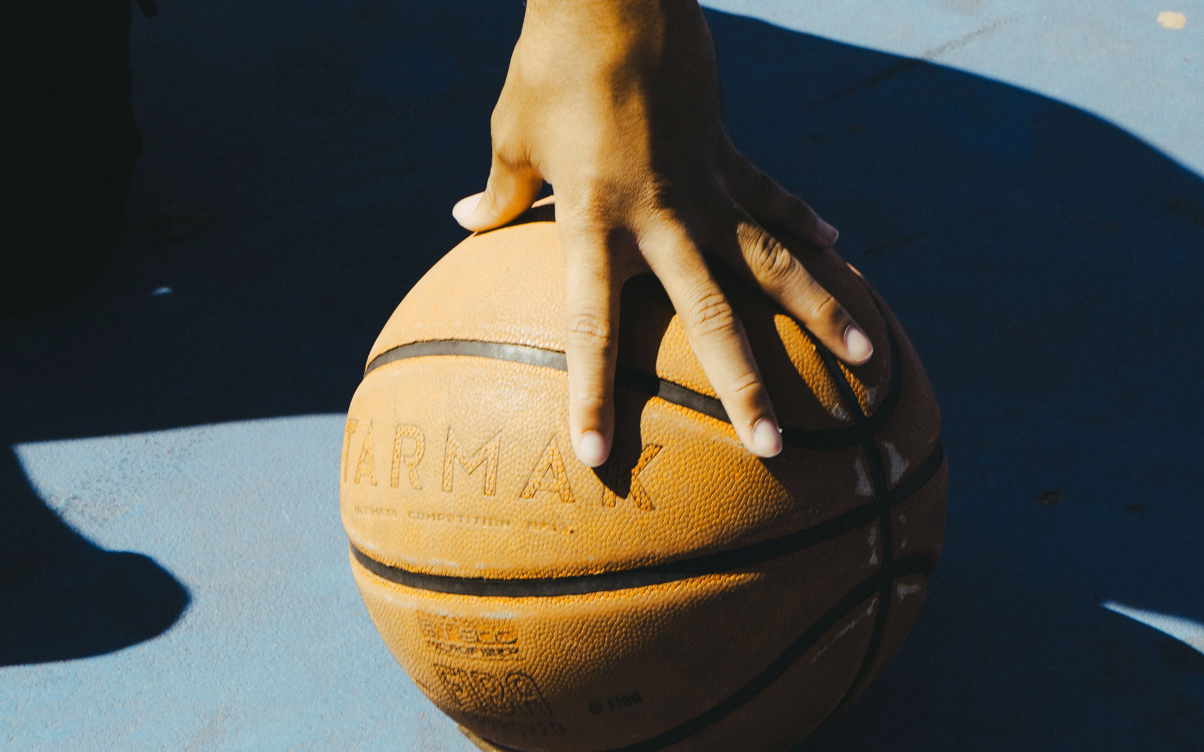 Hand liegt auf einem Basketball auf einem blauen Außen-Basketballplatz.