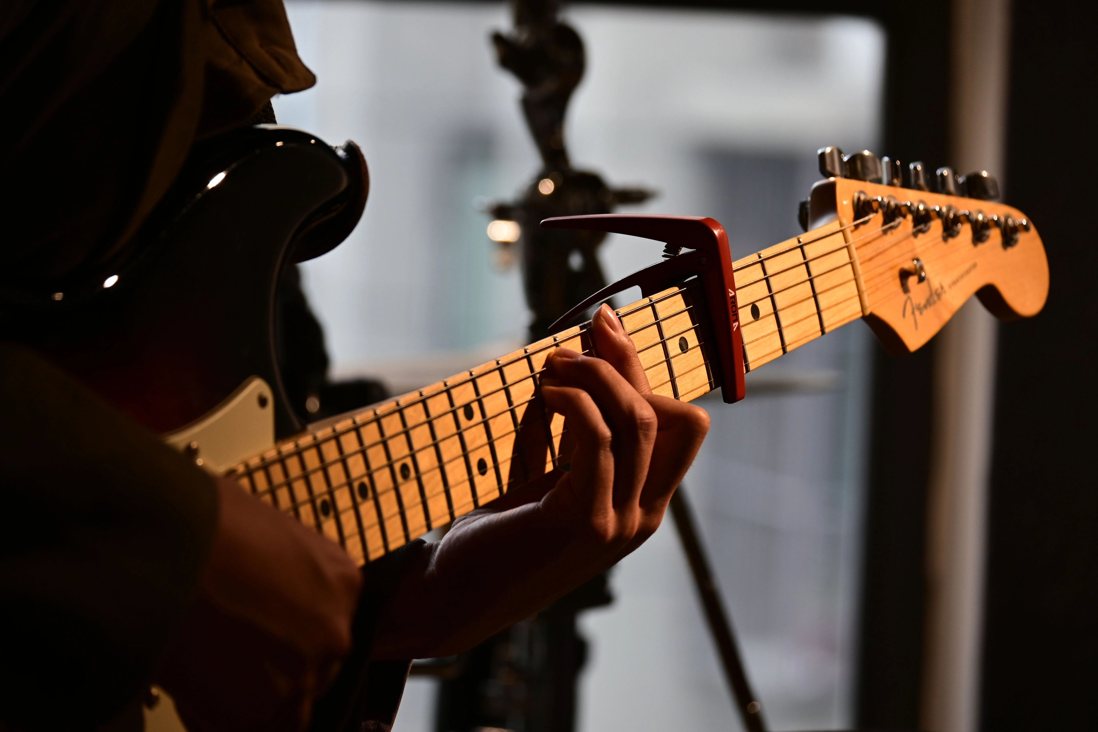 Nahaufnahme einer Hand, die auf dem Hals einer Fender-E-Gitarre mit Kapodaster Akkord greift.