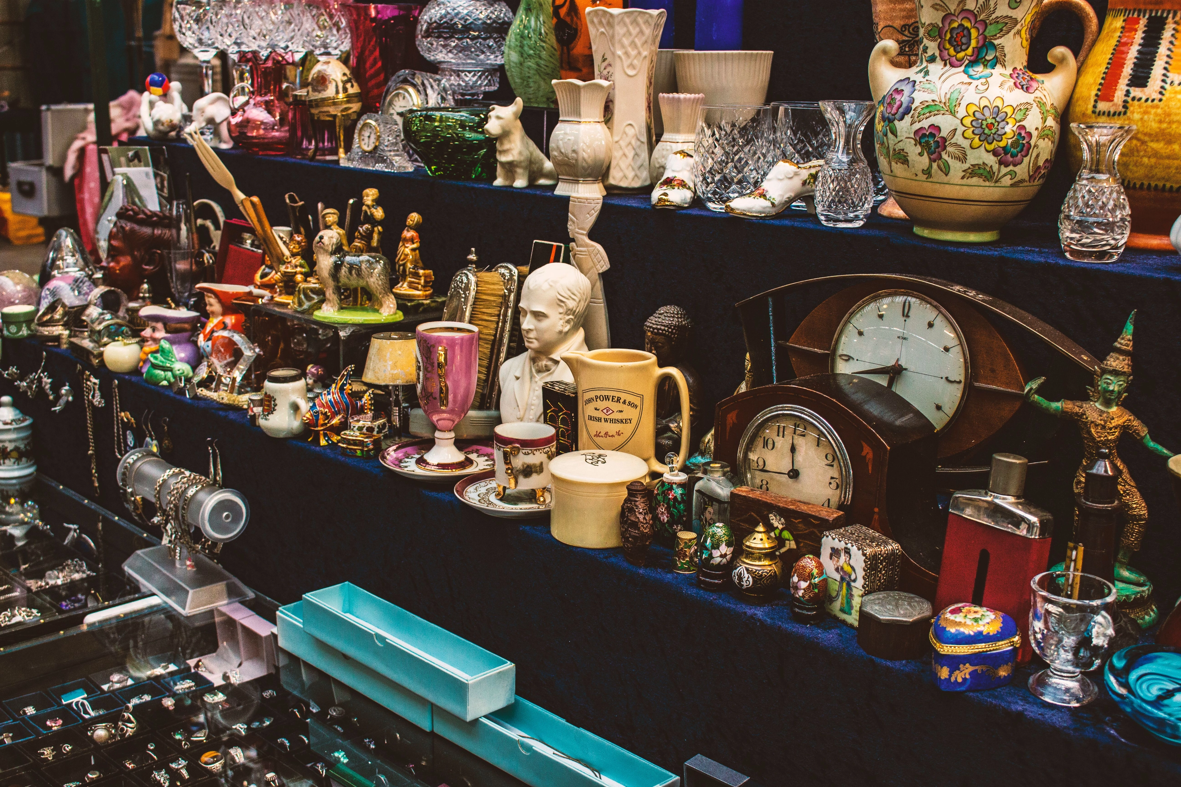 Tisch mit Antiquitäten und Trödel: Vasen, Uhren, Porzellanbüste, Schmuck und verschiedene Dekoobjekte auf Regalen.